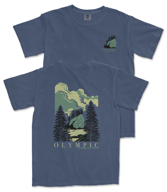 A blue t-shirt with a graphic design depicting a mountain landscape with pine trees and clouds.