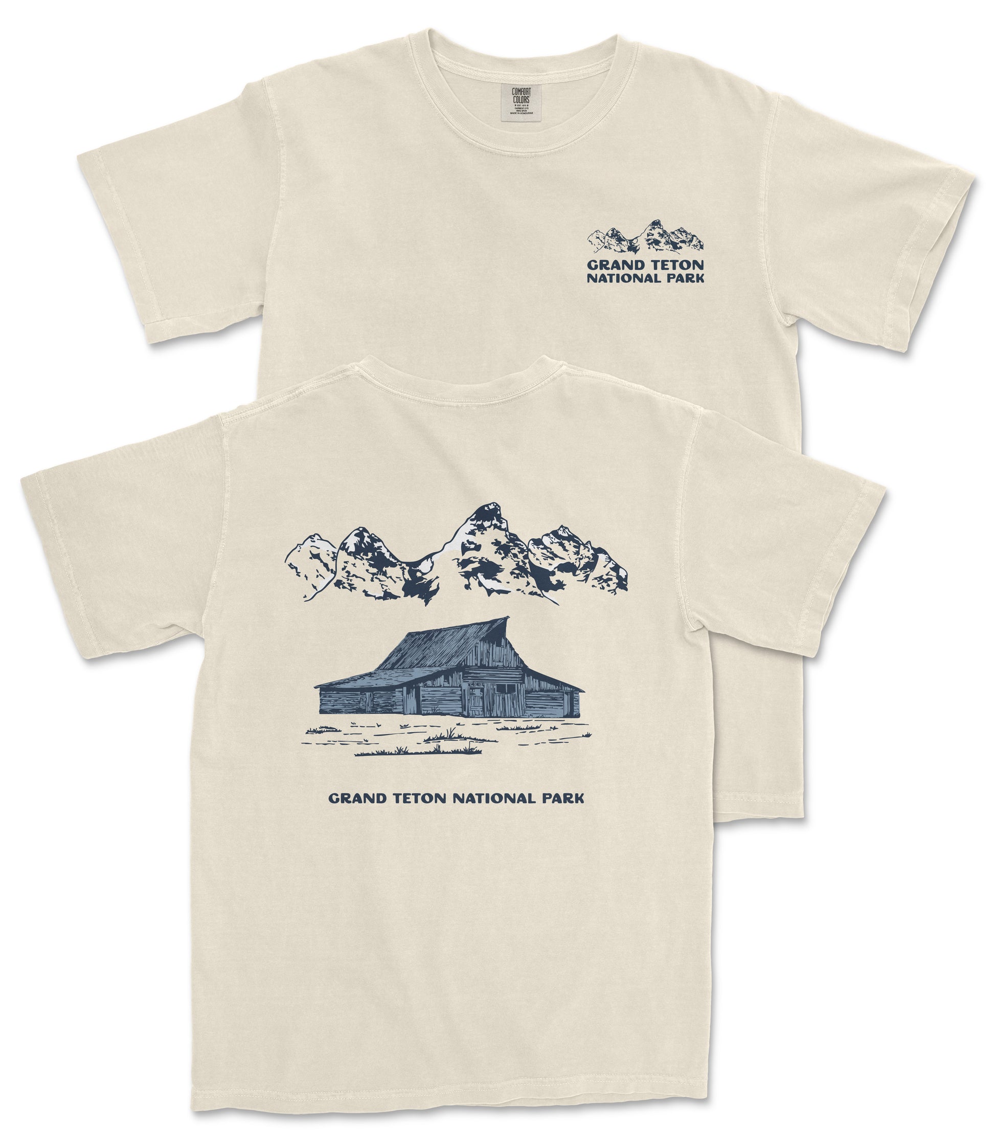 A beige t-shirt with a graphic design depicting a cabin and mountains, along with the text "Grand Teton National Park" printed on the back.