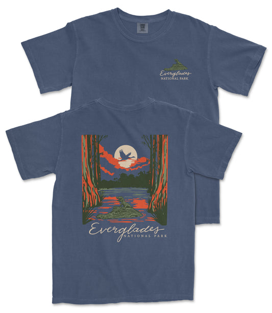 a blue t-shirt with a graphic design depicting a serene landscape with a lake, a bird, and a sunset. The text on the t-shirt reads "EVERGLADES NATIONAL PARK".