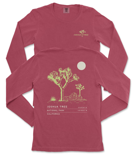 a red long-sleeved t-shirt with a graphic design depicting a desert landscape, including a tree and a moon. The text on the t-shirt reads "JOSUA TREE 33.87°N, 115.907°W, CALIFORNIA".