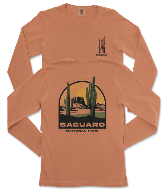 a long-sleeved orange t-shirt with a graphic design depicting a desert landscape with a cactus and mountains in the background. The text "SAGUARO NATIONAL PARK" is printed on the back of the shirt.
