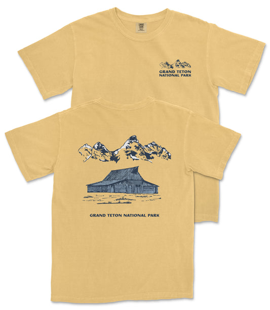 A yellow t-shirt with a graphic design depicting a cabin and mountains, along with the text "Grand Teton National Park".