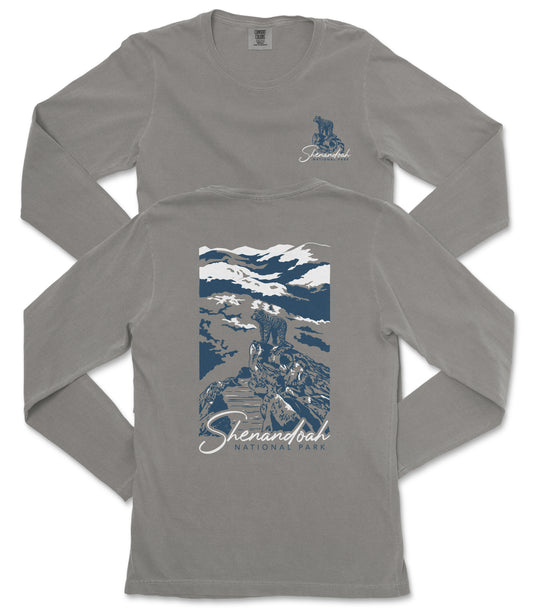 a gray long-sleeved t-shirt with a graphic design on the back. The design depicts a mountain landscape with a person standing on a rock. The text "Shenandoah National Park" is printed below the graphic.
