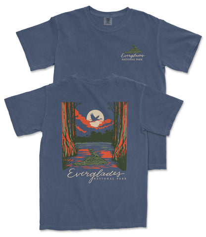 a blue t-shirt with a graphic design depicting a serene landscape with a lake, a bird, and a sunset. The text on the t-shirt reads "EVERGLADES NATIONAL PARK".