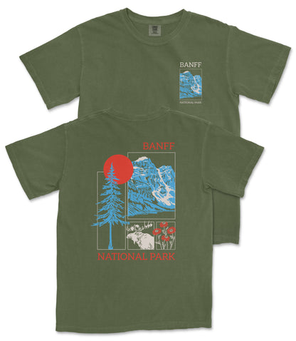 a green t-shirt with a graphic design depicting a mountain landscape, including a pine tree, a red sun, and various wildlife elements.