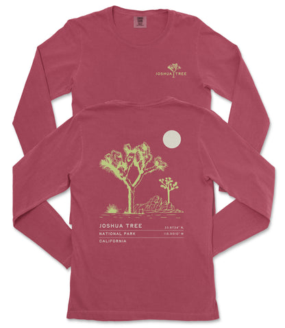 a red long-sleeved t-shirt with a graphic design depicting a desert landscape, including a tree and a moon. The text on the t-shirt reads "JOSUA TREE 33.87°N, 115.907°W, CALIFORNIA".