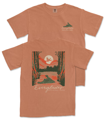 a t-shirt with a graphic design depicting a serene natural scene, including a lake, trees, and a bird.
