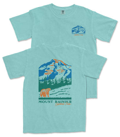 A light blue t-shirt with a graphic design depicting a mountain landscape, including a mountain peak, trees, and a bear. The text "MOUNT RAINER" and "National Forest" is printed on the t-shirt.