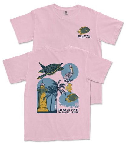 A pink t-shirt with a graphic design featuring a lighthouse, palm trees, and various marine life, including a fish and a turtle.