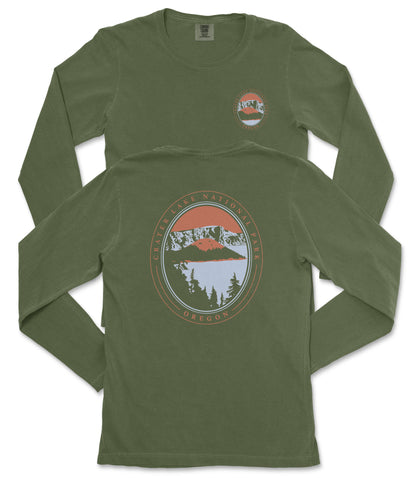 a pair of olive green long-sleeved t-shirts with a graphic design on the back. The design features a circular emblem with a mountain landscape and a lake, surrounded by a border with the text "CASTER LAKE NATIONAL PARK OREGON" printed on it.
