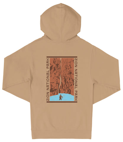 A beige hooded sweatshirt with a graphic design on the back, depicting a person standing in front of a waterfall.