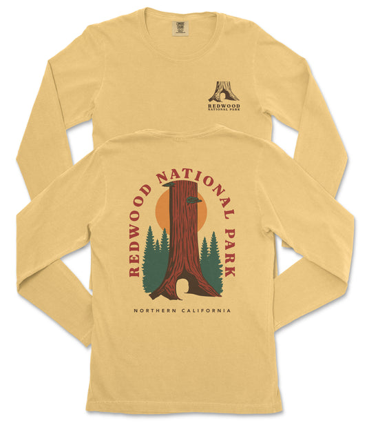 a yellow long-sleeved t-shirt with a graphic design depicting a tall tree with a sun-like symbol above it, surrounded by pine trees. The design also includes the text "REDWOOD NATIONAL PARK NORTHERN CALIFORNIA".