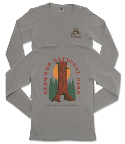 a gray long-sleeved t-shirt with a graphic design depicting a tall tree with a sun-like symbol in the center, surrounded by green trees and mountains. The design is related to Redwood National Park in Northern California.