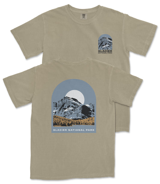 a beige t-shirt with a graphic design depicting a mountain landscape with a full moon. The design includes the text "Glacier National Park" and "Glacier" along with a mountain silhouette.