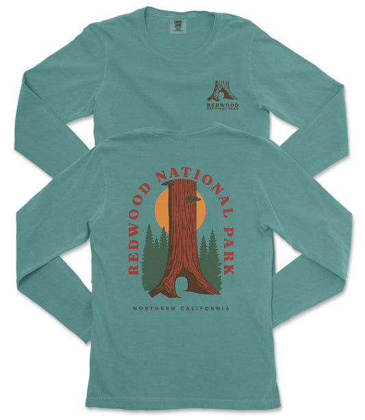 A long-sleeved green t-shirt with a graphic design featuring a tree trunk and a sunset, along with the text "REDWOOD NATIONAL PARK NORTHERN CALIFORNIA".