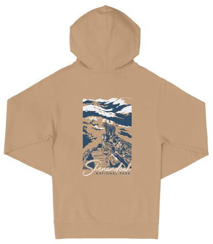 A beige hooded sweatshirt with a graphic design on the back depicting a mountain landscape with a person standing on a rock.