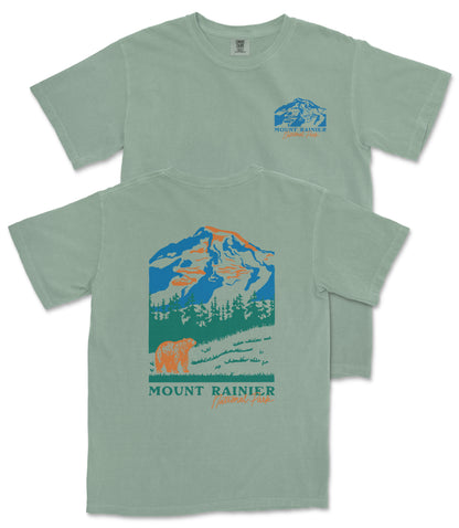 A green t-shirt with a graphic design depicting a mountain landscape, including a bear and trees, along with the text "Mount Rainier National Forest".